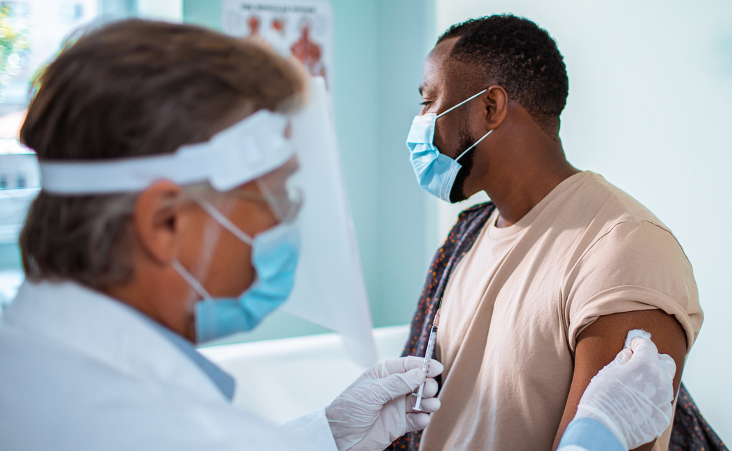 Masked clinician prepares to administer vaccine to patient.