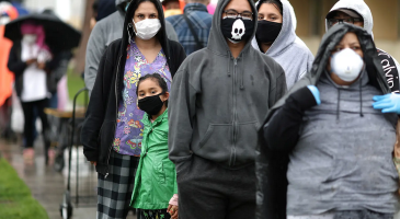 People wait in line outside food bank, wearing protective masks