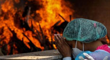 Masked woman prays before cremation site in India.