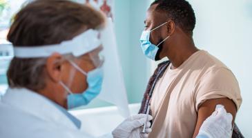 Masked clinician prepares to administer vaccine to patient.