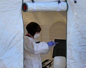 Healthcare worker standing inside door of tent wearing mask and protective gear and looking down at clipboard in hands