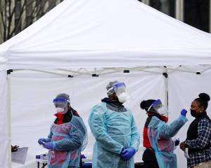 Masked and gowned health workers conduct COVID test in outdoor tent.