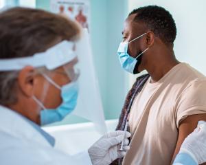 Masked clinician prepares to administer vaccine to patient.