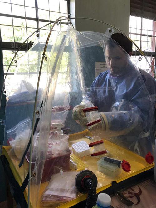 CDC biologist works on mobile biocontainment unit wearing protective gear