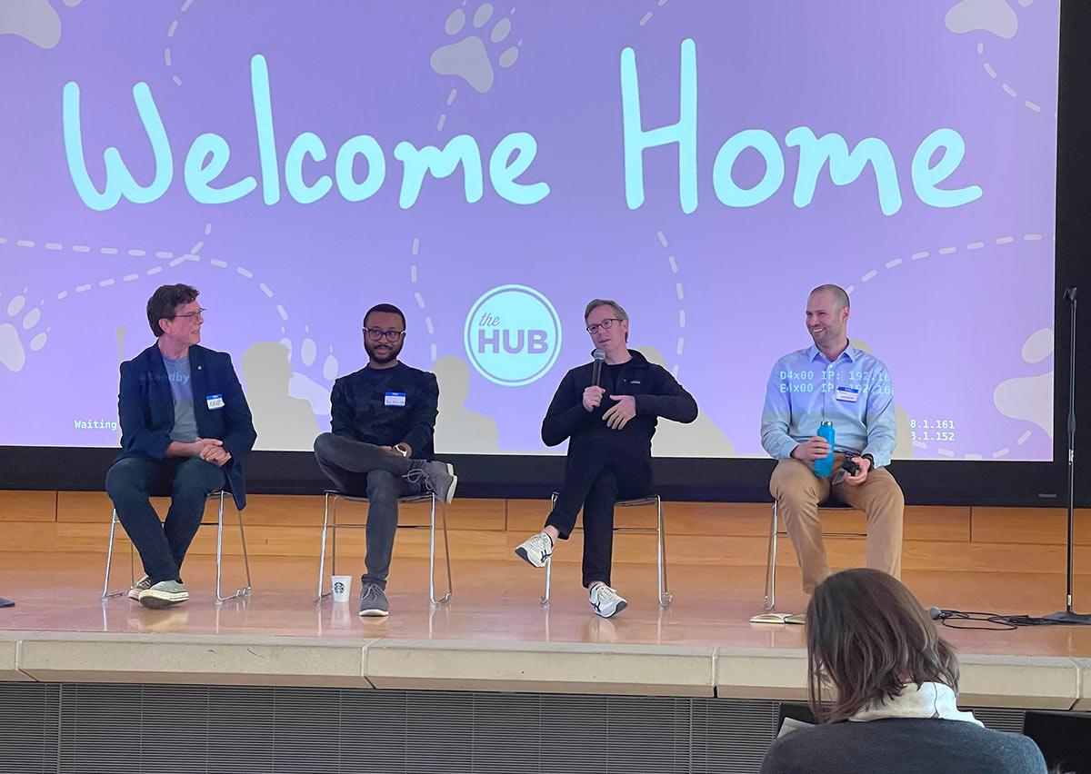 Four alumni sit on a stage with microphone, answering questions from the audience